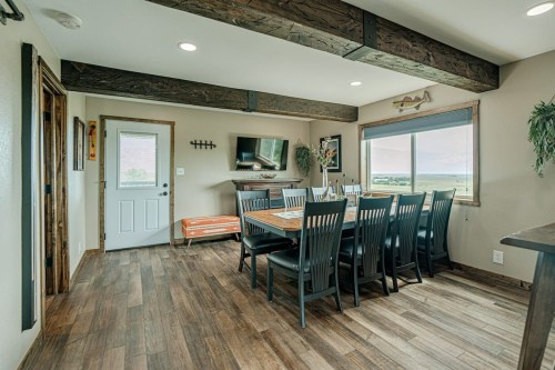 A spacious dining area with a large table, black chairs, wooden beams, and a view of the outdoors through a window.