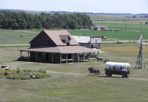 A rustic farm scene featuring a large barn, a wagon with horses, and green fields in the background.
