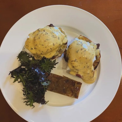 A plate with two eggs Benedict topped with hollandaise sauce, accompanied by greens and a rectangular piece of jelly.