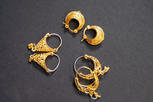 Four pairs of intricate gold earrings displayed on a dark background, showcasing various designs and textures.