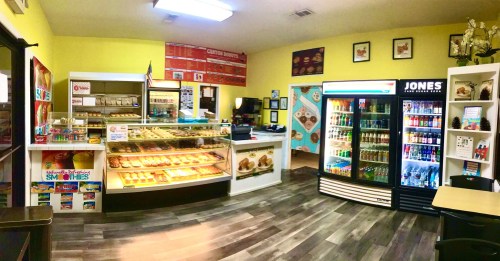 A colorful interior of a small shop featuring a display case of pastries, a drink fridge, and a menu board on the wall.