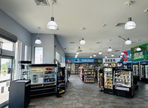 Interior of a convenience store with shelves of snacks, drinks, and a display case, brightly lit with hanging lights.