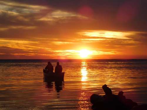 Two people in a small boat silhouetted against a vibrant sunset over calm waters.