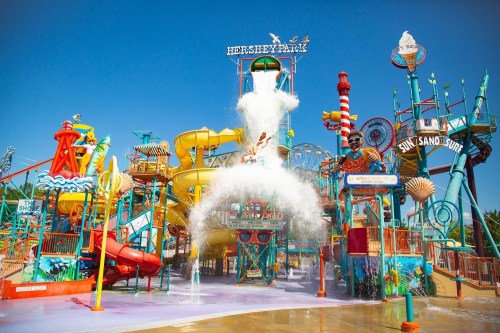 Colorful water park with slides and a large splash feature under a clear blue sky. Fun and vibrant atmosphere.