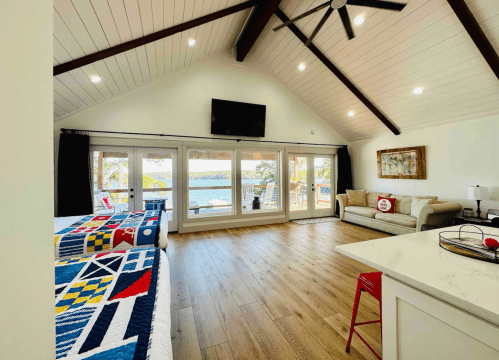 Bright, modern living space with high ceilings, large windows, and a view of the water. Features a cozy seating area and beds.
