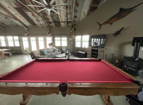 A rustic game room featuring a red pool table, cozy seating, and large windows with a view.