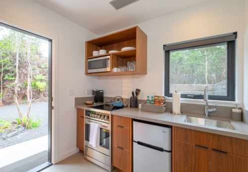Modern kitchen with wooden cabinets, stainless steel appliances, and a view of greenery through the open door.