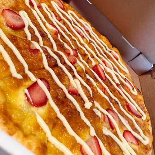 A pizza topped with strawberries and drizzled with a creamy sauce, presented in a pizza box.