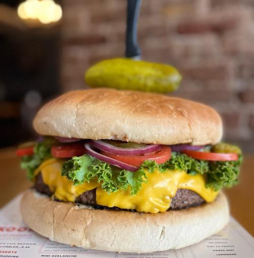 A large cheeseburger with lettuce, tomato, onion, and a pickle on top, served on a toasted bun.