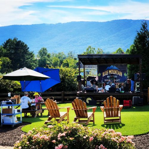 Outdoor stage at Blue Mountain Brewery with seating, umbrellas, and mountains in the background on a sunny day.