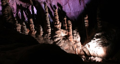 Stalactites and stalagmites illuminated in a dark cave, creating dramatic shadows and colorful highlights.