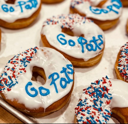 A tray of donuts with white icing, blue "Go Pats" writing, and red, white, and blue sprinkles.