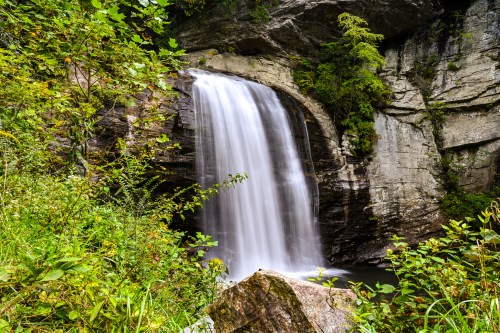 A serene waterfall cascading over rocky cliffs, surrounded by lush greenery and vibrant foliage.