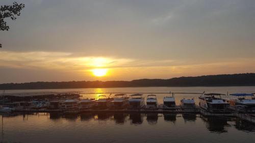 Sunset over a calm lake, with boats docked along the shore and trees silhouetted in the background.