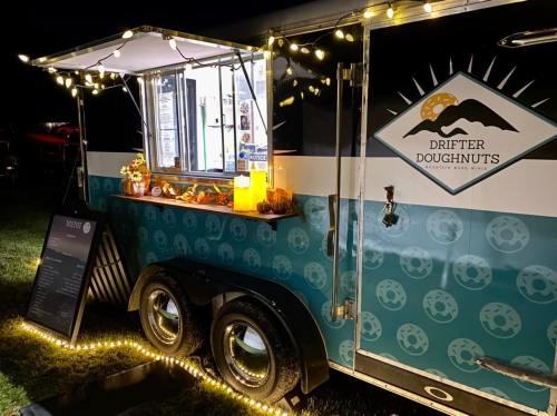 A brightly lit food truck at night, featuring a menu and decorative lights, serving Drifter Doughnuts.