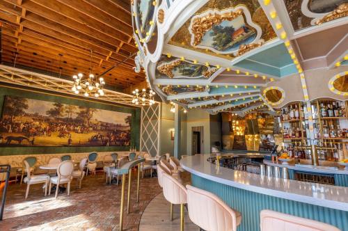 Elegant restaurant interior featuring a bar, ornate ceiling, and a large mural, with stylish seating and warm lighting.