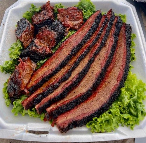 Sliced smoked brisket on a bed of lettuce, featuring a mix of charred and tender pieces.