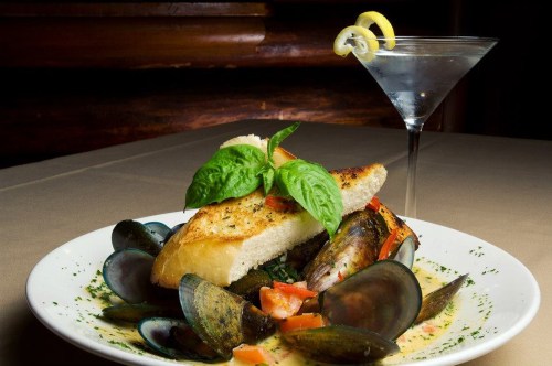 A plate of mussels with bread, garnished with basil and tomatoes, alongside a martini with a lemon twist.