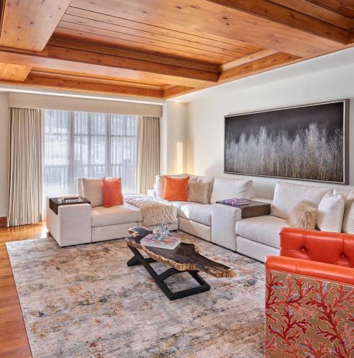Cozy living room with wooden beams, a plush sofa, colorful pillows, and a rustic coffee table on a patterned rug.