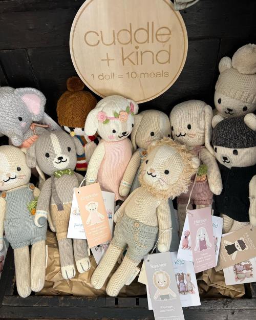 A collection of knitted dolls in various designs, displayed with a sign that reads "cuddle + kind, 1 doll = 10 meals."