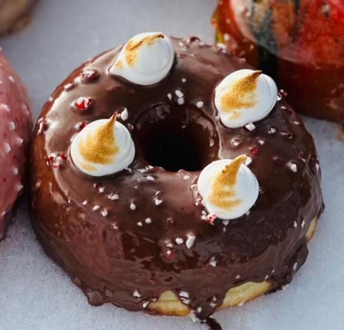 A chocolate frosted donut topped with four toasted meringue peaks and sprinkled with crushed peppermint.