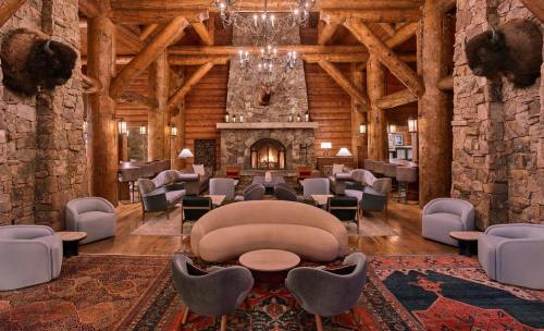 Cozy lodge interior with stone walls, wooden beams, plush seating, and a central fireplace, adorned with rustic decor.