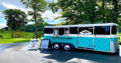 A colorful food truck parked in a scenic area, offering doughnuts, with a menu displayed outside.