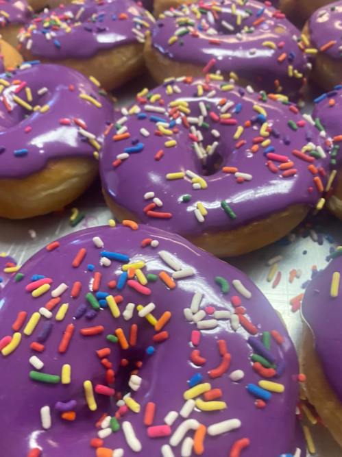 A close-up of purple frosted donuts topped with colorful sprinkles, arranged on a tray.