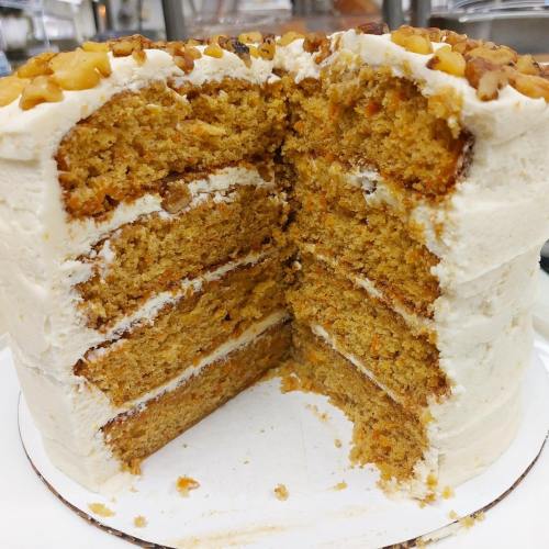 A layered carrot cake with cream cheese frosting and walnuts, partially sliced to reveal its moist interior.