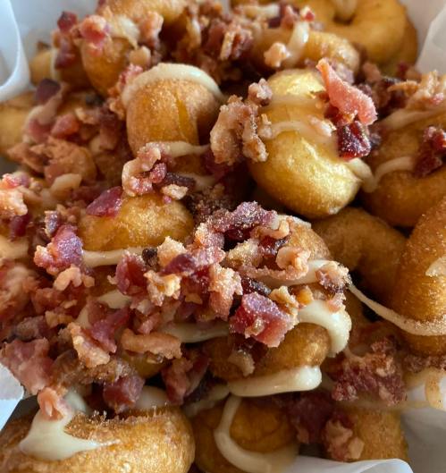 A close-up of golden, bite-sized donuts topped with crispy bacon bits and a drizzle of creamy sauce.