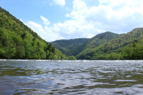 A serene river flows between lush green mountains under a partly cloudy sky.