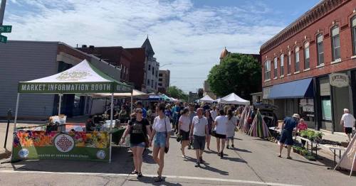 A bustling street market with booths, tents, and people shopping on a sunny day.