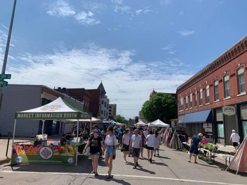 A bustling street market with tents, booths, and people walking under a clear blue sky.