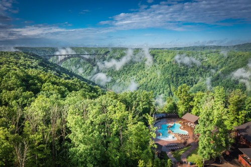 A scenic view of lush green mountains with a pool area below and a bridge spanning the valley in the background.