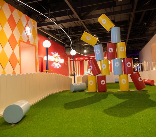 Colorful stacked cups in a playful indoor space with artificial grass and whimsical decor.