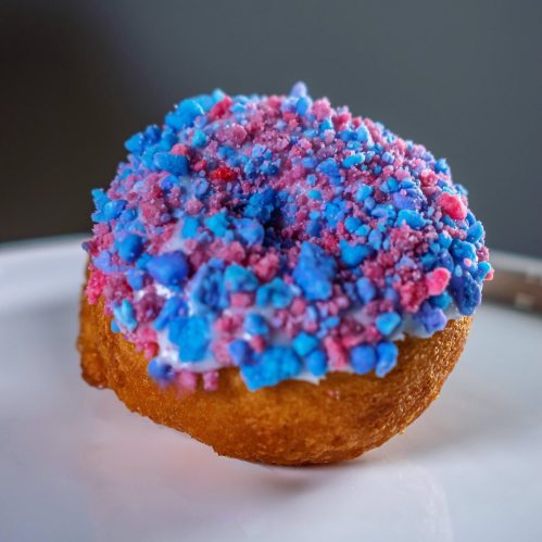 A colorful donut topped with blue and pink sprinkles on a white plate.