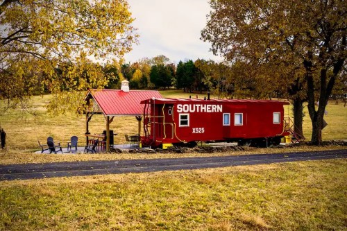 A red train caboose with "SOUTHERN" written on it, set in a grassy field with autumn trees and a nearby gazebo.