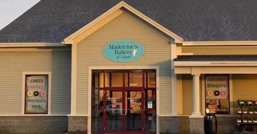 Exterior of Madeleines Bakery, featuring a sign and large windows displaying baked goods like cakes and pastries.