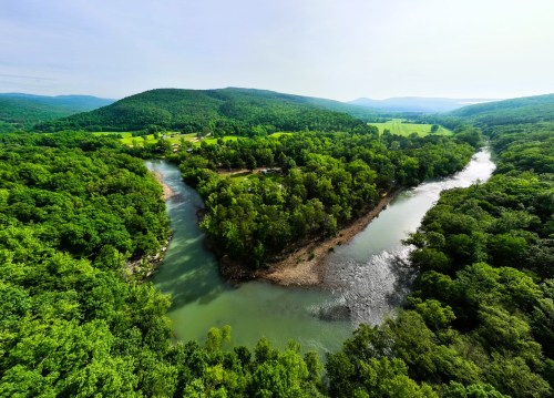 Aerial view of a winding river surrounded by lush green forests and rolling hills under a clear sky.