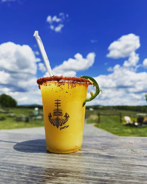 A refreshing yellow drink with a chili rim and lime garnish, set against a bright blue sky and green landscape.