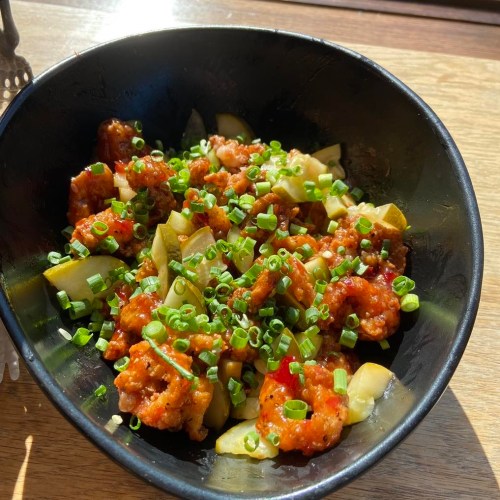 A black bowl filled with diced vegetables and shrimp in a spicy sauce, topped with chopped green onions.