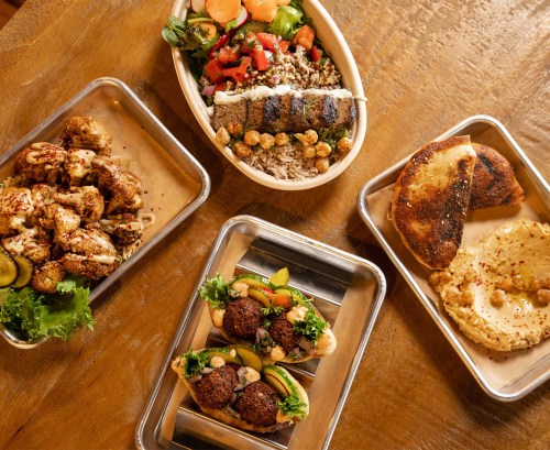 A spread of Mediterranean dishes including falafel, salad, hummus, and pita on metal trays.