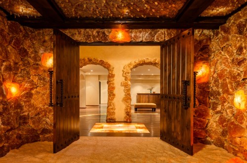 A warmly lit entrance with wooden doors, stone walls, and glowing salt lamps, leading into a serene interior space.