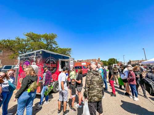 A busy food truck at an outdoor market, with a crowd of people waiting in line under a clear blue sky.
