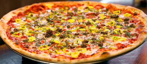 A large pizza topped with cheese, ground meat, yellow peppers, and herbs on a golden crust.