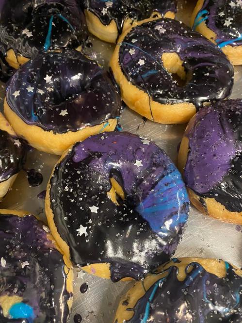 A close-up of colorful donuts with black and purple icing, decorated with star-shaped sprinkles.