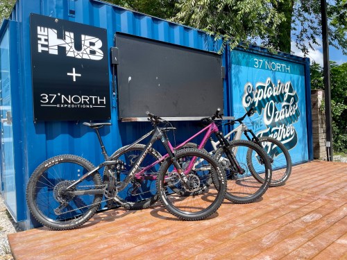Three mountain bikes parked in front of a colorful shipping container with signs for "The Hub" and "37 North Expeditions."
