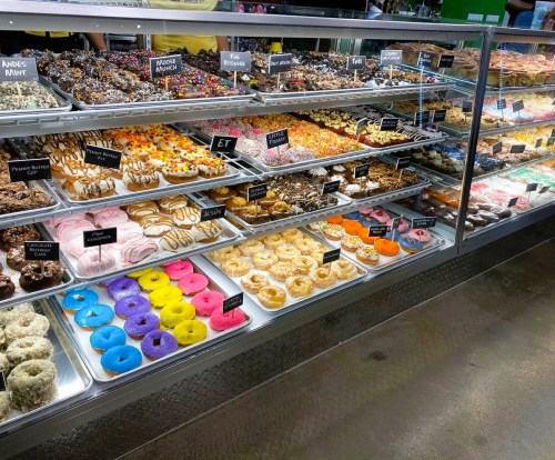 A display case filled with a variety of colorful pastries, donuts, and sweets, labeled with small signs.