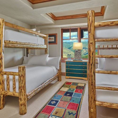 Cozy bedroom featuring a bunk bed, a queen bed, a colorful rug, and a scenic view through a large window.
