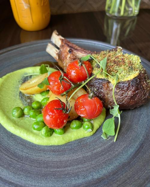 A plate featuring a lamb chop with herb crust, cherry tomatoes, peas, and a vibrant green puree.